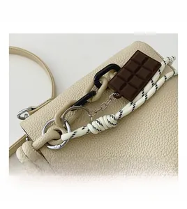 Gros plan du sac seau en cuir beige avec breloque chocolat et détails de chaînes