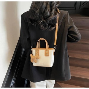 Detail of cream and brown crossbody bag showing the adjustable strap and plush charm