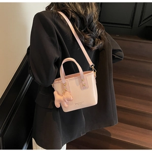 Detail view of pink mini bucket bag worn crossbody with cute plush puppy charm accessory