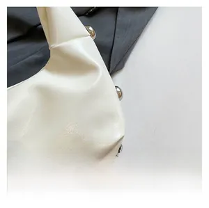 Detail view of white wrinkled leather surface with silver rivets on minimalist shoulder bag