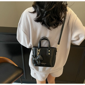 Detail of black crossbody bucket bag with gold lettering and dog charm on a model