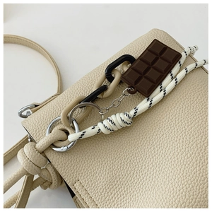 Détail d'un sac en cuir beige avec pendentif chocolat et bandoulière en corde tressée