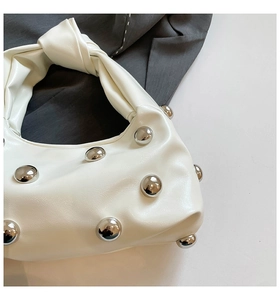 Detail of white studded hobo bag with silver rivets and knotted handle on grey fabric