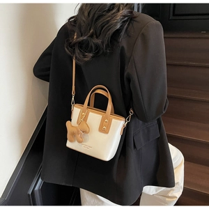 Chic beige bucket bag with brown trim and cute dog charm shown on a model outfit