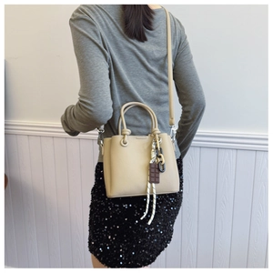 Détail du sac seau beige à motif litchi avec breloque en corde tressée et texture de cuir