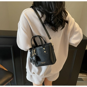 Detail of a black bucket bag with gold rivets and a decorative bow charm shown on model