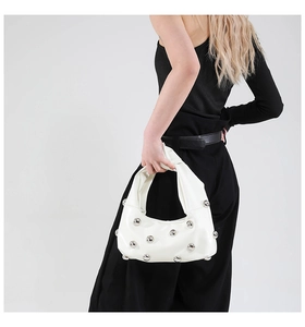 Detail view of white half-moon bag featuring silver metal studs and matte leather finish