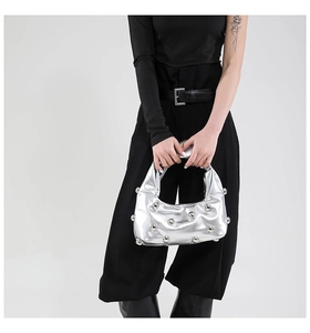 Detail of metallic silver underarm bag with decorative rivets on soft pleated leather