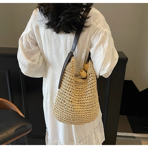 Detail of hand-woven beige straw bag with adjustable brown leather strap on white dress