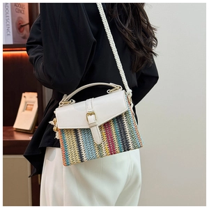 Close-up of a colorful woven straw beach bag with white leather straps and tassel detail