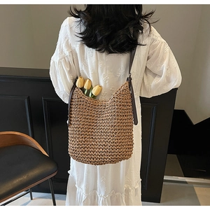 Detail of hand-woven straw shoulder bag with leather strap on white lace dress