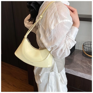 Detail showing the light yellow patent leather texture and crescent shape of the handbag