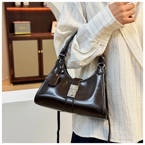 Detail of a dark brown patent leather pleated handbag with a silver square buckle