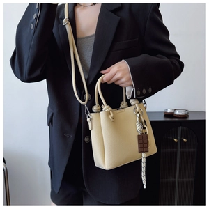 Détail du sac seau beige en cuir grainé avec breloque chocolat sur la bandoulière réglable
