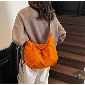 Detail of waterproof orange nylon crossbody bag with drawstring closure on a model