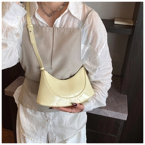 Close-up of glossy light yellow patent leather crescent bag with adjustable shoulder strap