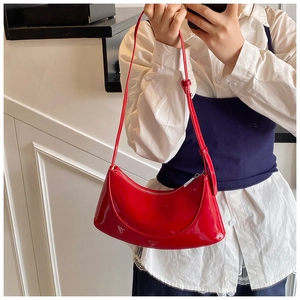 Model wearing a bright red patent leather crescent bag with high gloss mirror finish