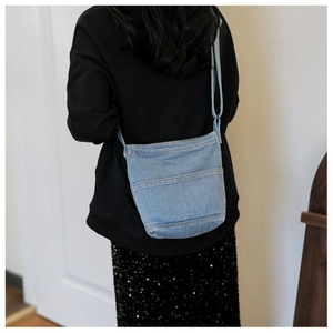 Détail du sac à bandoulière en jean bleu clair avec poches superposées porté par le modèle