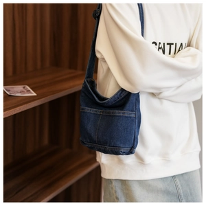 Gros plan d'un sac hobo en denim bleu foncé avec surpiqûres orange contrastées sur l'épaule
