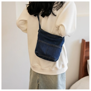 Détail d'un petit sac bandoulière en denim avec coutures jaunes sur la poche extérieure