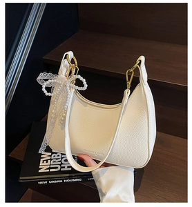 Détail du sac hobo en cuir grainé blanc avec nœud en perles et fermeture dorée sur bois sombre