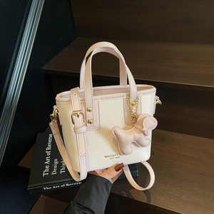 Pink and white mini leather crossbody bucket bag with dog charm on wooden stairs