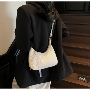 Sac demi-lune en cuir blanc grainé avec breloque nœud en perles porté à l'épaule