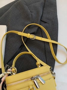 Yellow leather vanity bag with top handle and shoulder strap on grey blazer background