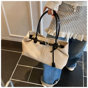 Detail of beige woven tote bag with black leather straps and silver buckle closure