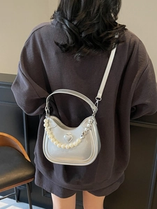 Zilveren crossbodytas met hartdecoratie en parelketting gedragen door een model