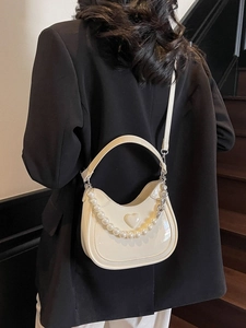 Crèmewitte zadeltas met parelketting en 3D-hartdetail op model met een zwarte blazer