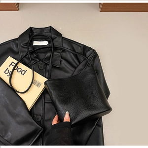 Detailed view of black litchi grain leather bucket bag on a stylish dark jacket