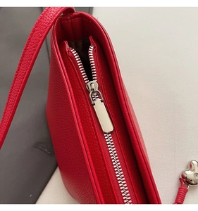 Close-up of red lychee leather bag with silver zipper and heart pendant detail