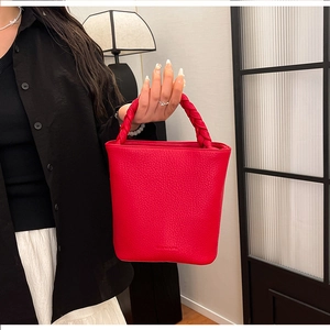 Detail of red pebbled leather bucket bag featuring a unique thick woven handle design
