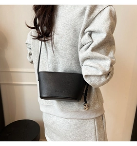 Detail view of black litchi pattern leather bucket bag with silver charm and shoulder strap