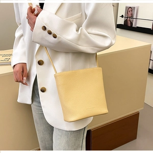 Close-up of minimalist cream leather bucket bag with lychee grain on a female model
