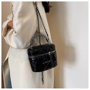 Close-up of black quilted mini box bag with chain straps on light trench coat