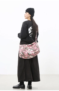 Detail view of large pink camouflage canvas crossbody bag worn by model in casual style