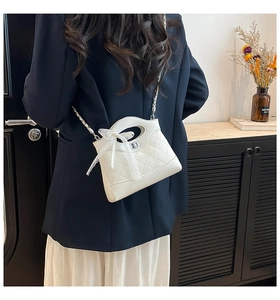 Close-up of white quilted chain bag featuring a lace bow and metallic twist lock