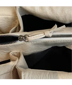 Close-up of silver metal zipper and litchi texture leather detail on beige tote bag