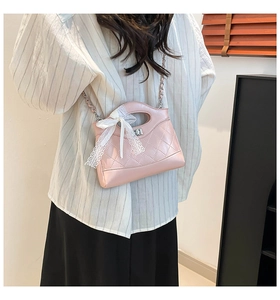 Detailed view of pink quilted handbag with white lace bow on a crossbody chain strap