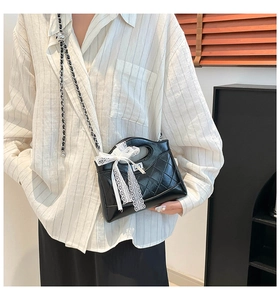 Detail of black quilted bucket bag with lace bow and chain strap in indoor setting