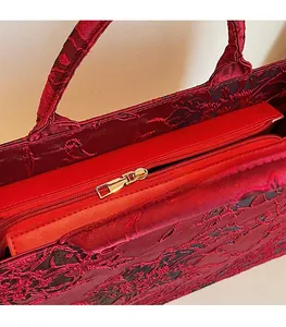 Close-up of the smooth golden metal zipper and red floral jacquard fabric on the handbag