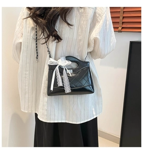 Close-up of quilted black handbag featuring white lace bow detail and silver chain strap