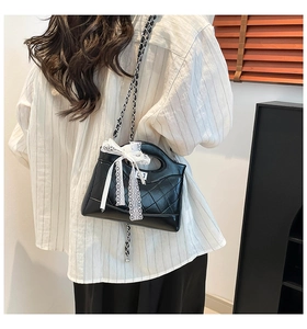 Detail of quilted black shoulder bag featuring a white lace bow and metal chain strap