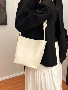 Creamy white leather bucket bag with knotted shoulder strap and minimalist design
