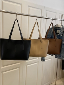 Three minimalist leather tote bags in black, beige, and brown hanging on a metal rack
