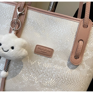 Detail of white snakeskin tote bag with pink leather trim and cloud plush pendant