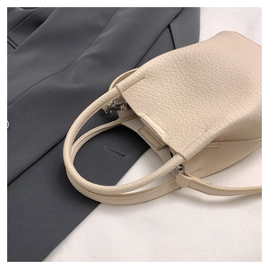 Close-up of cream lychee texture leather bucket bag against a dark grey blazer