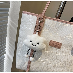 Close-up of a white plush cloud charm with striped legs hanging on a white handbag
